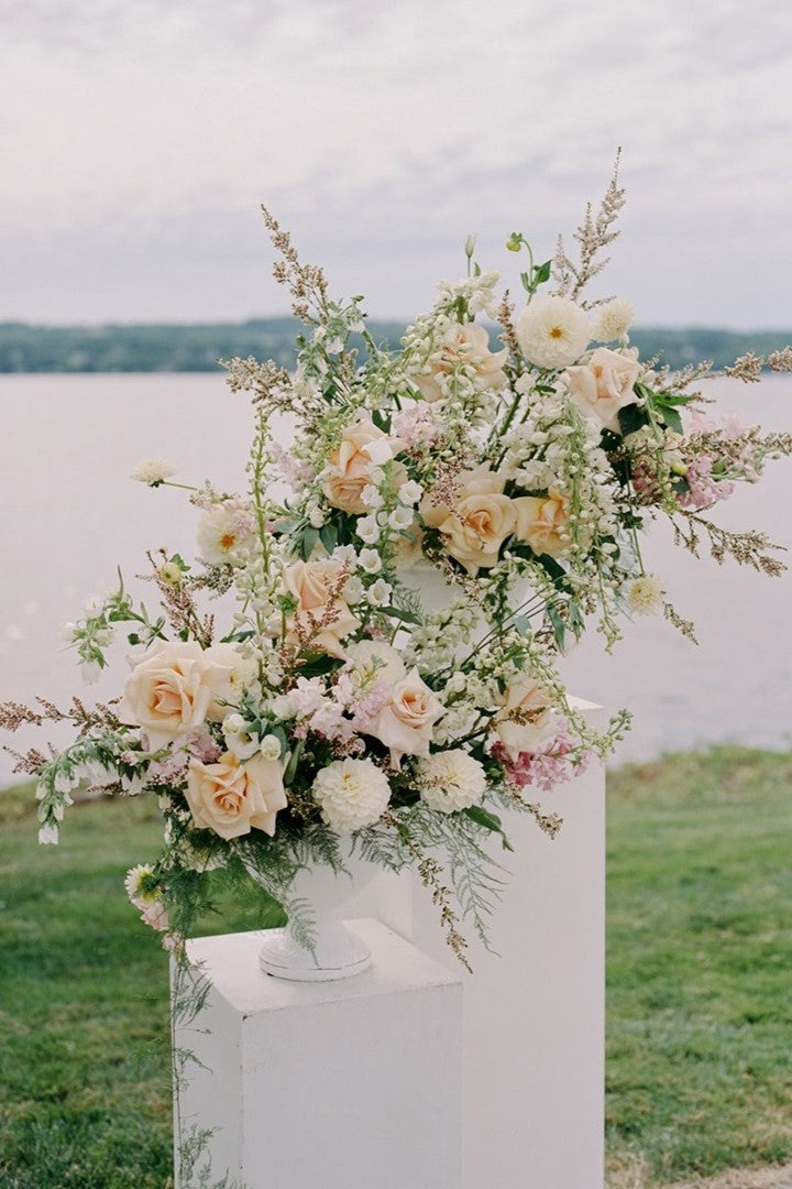 Large floral arrangements with a variety of textures and florals. Colors are white, peach, and pink, with green accents. Some flowers included are roses, dahlias, and snapdragons.