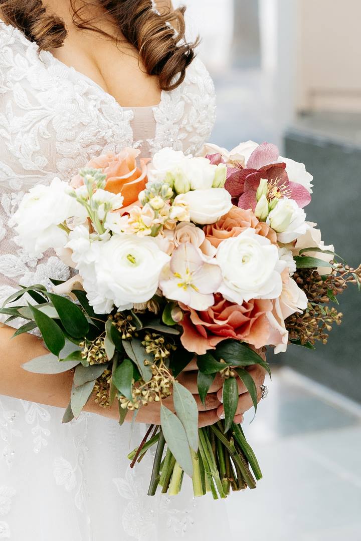 A bridal bouquet with roses, seeded eucalyptus and more. White, orange, purple, and blush.