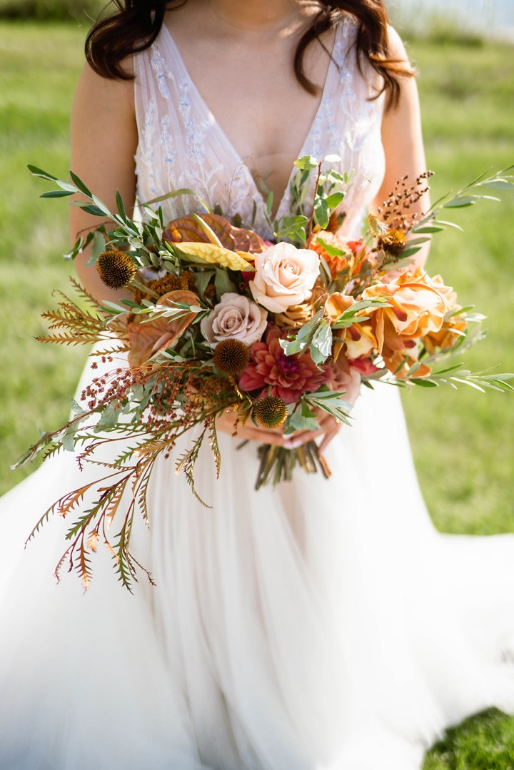 Bride holding a fall colored bouquet with oranges, greens, light pinks, and browns.