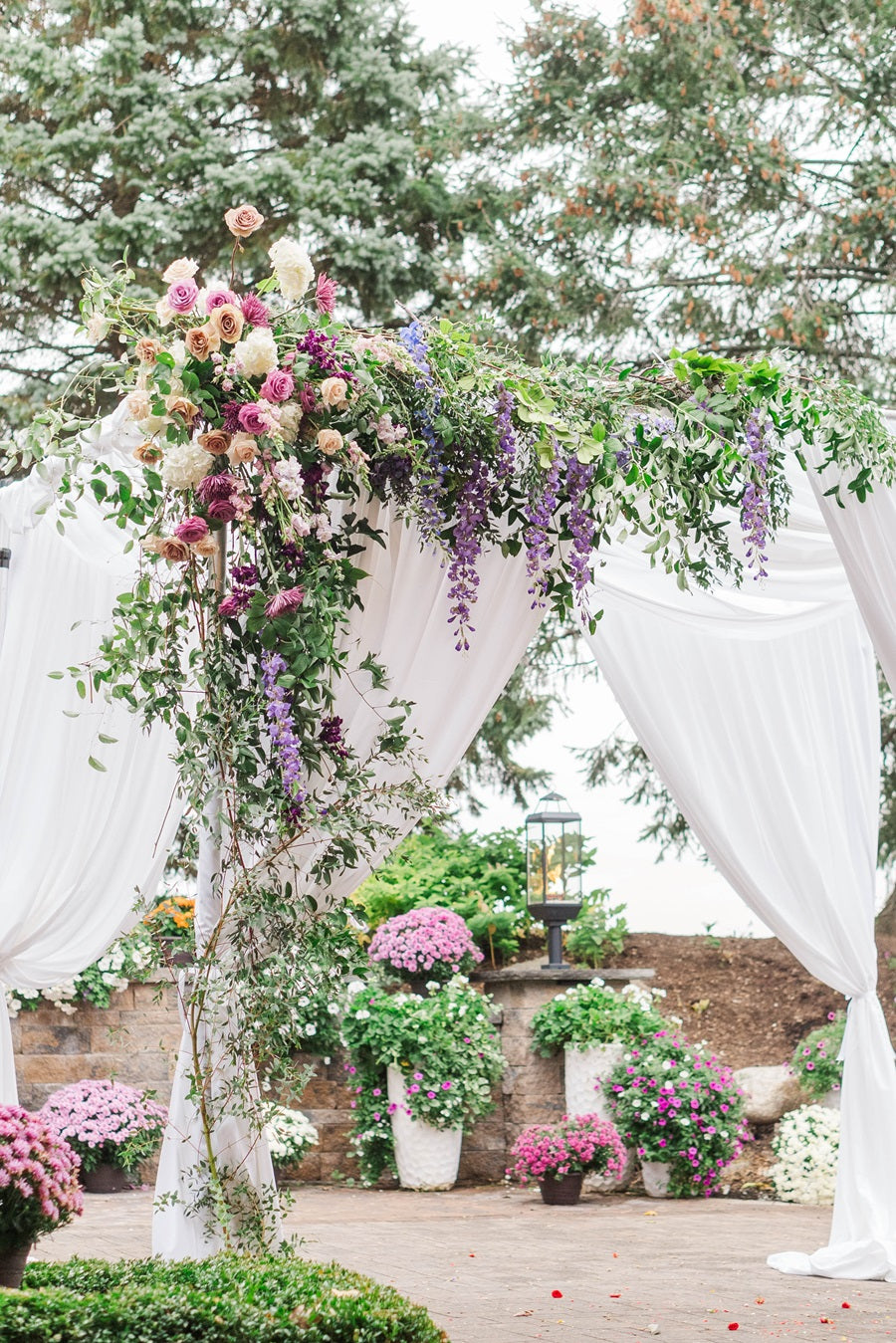 Close up on the floral that fills the upper left of the chuppah. It is lush with greenery and florals in a nice spring palette of pink, purple, white, and green.