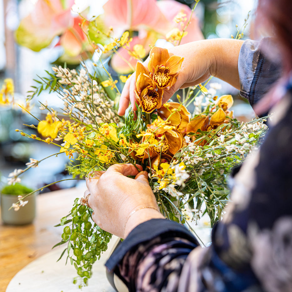 Person making an arrangement with yellow orchids at Stacy K Floral in Rochester NY