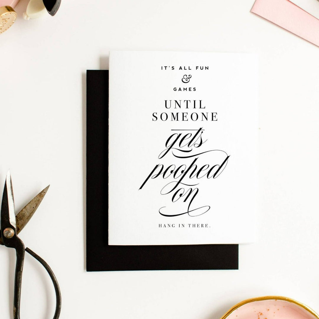 A simple white card with text that reads "It's all fun & games until someone gets pooped on, hang in there." Comes with a black envelope.