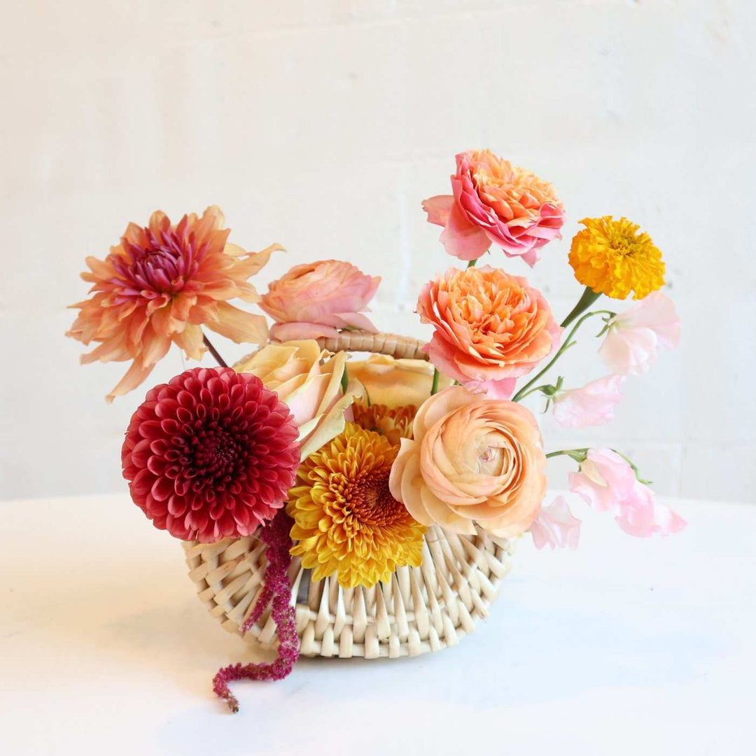 fall basket with orange dahlias, bronze mums, ranunculus, marigolds, light pink sweet pea, and peach roses.