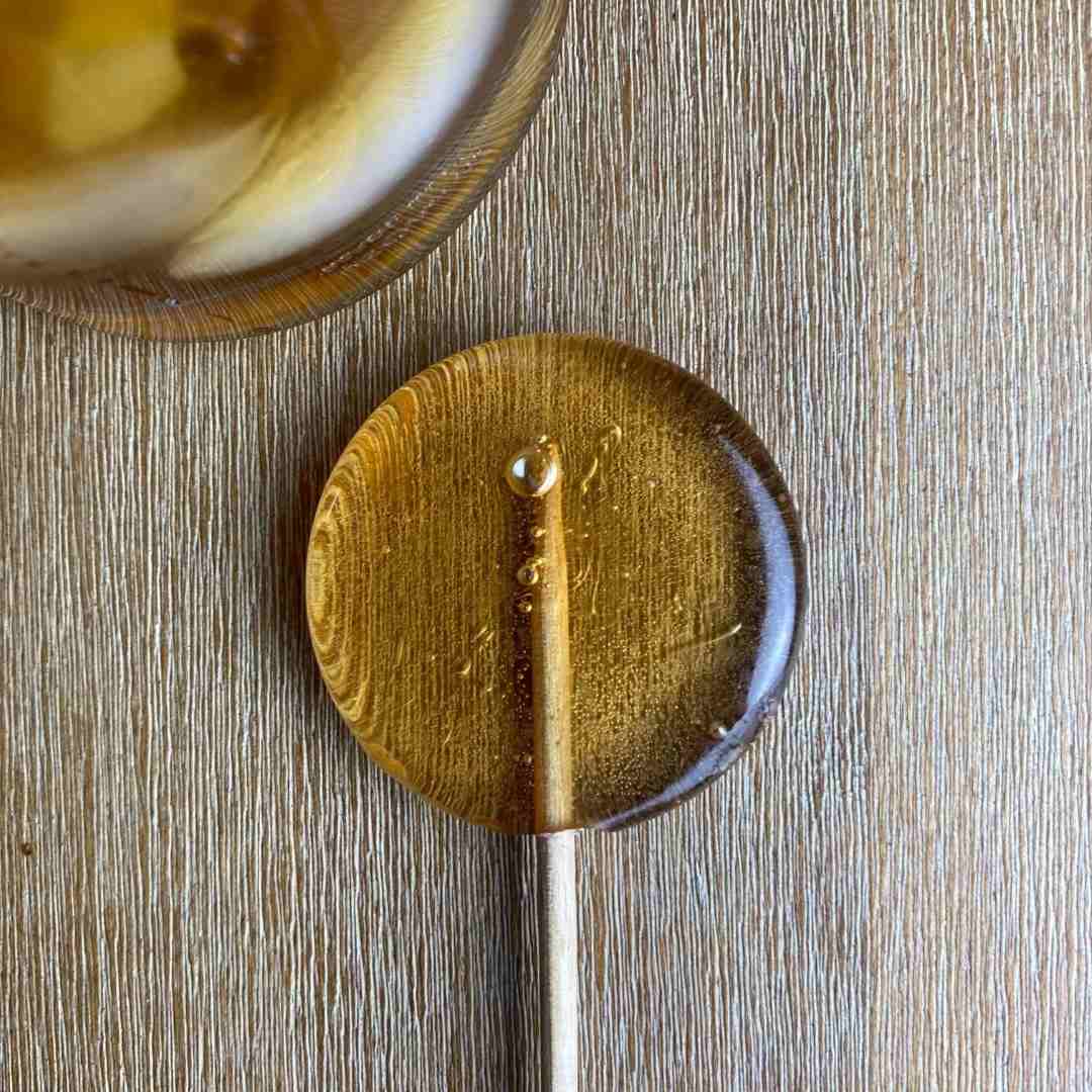A yellow/orange transparent lollipop against a gray background | Bourbon lollipop