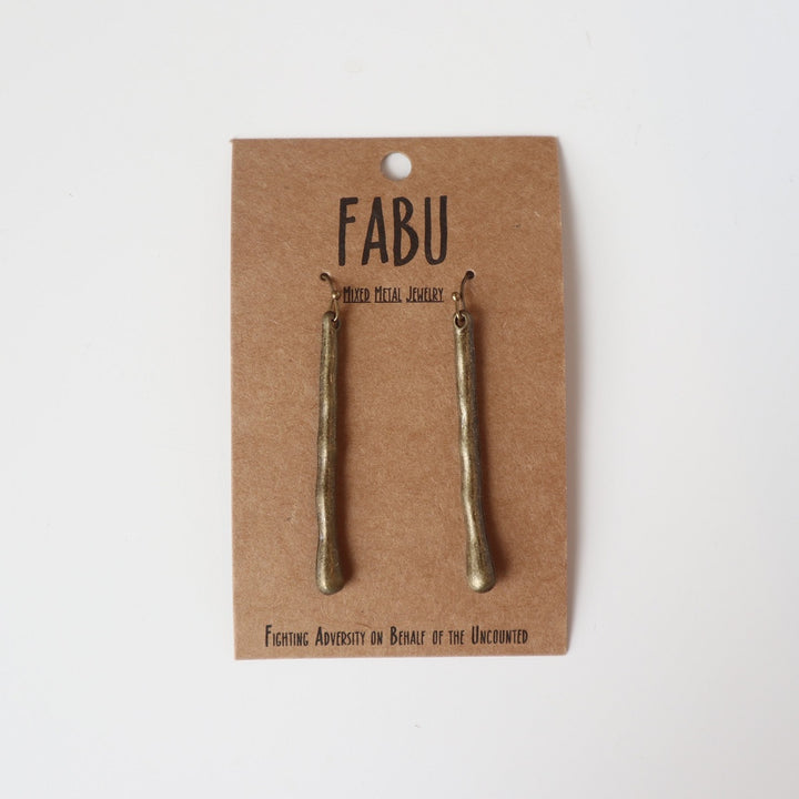 Fabu Earrings | Bronze dangling earrings in the subtle shape of a twig.  On a brown paper backing. Reads "Fabu, mixed metal jewelry, Fighting Adversity on Behalf of the Uncounted".