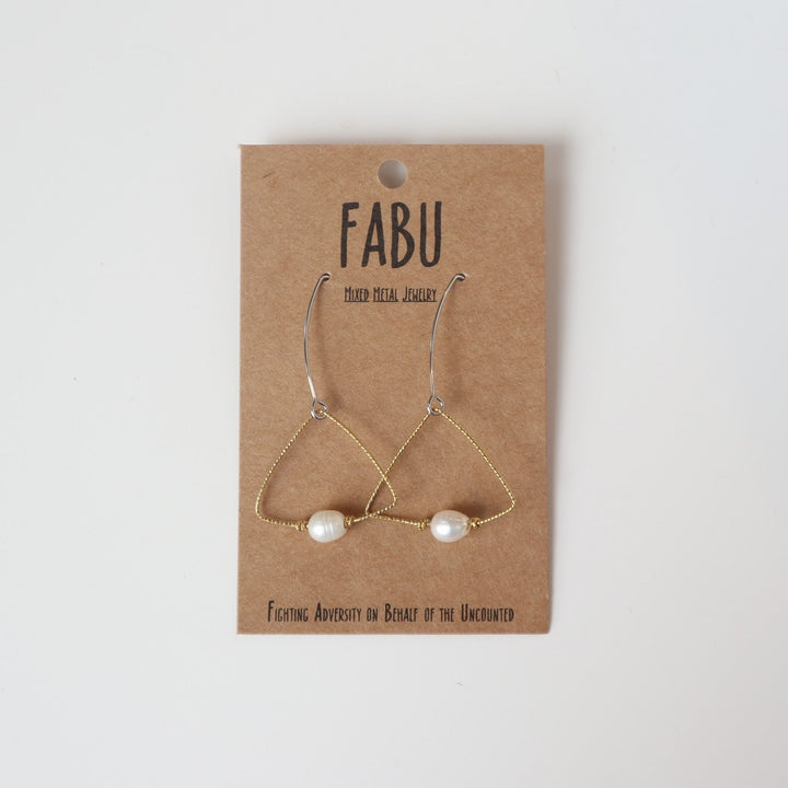 Fabu Earrings | A gold wire earring shaped like a triangle that has a pearl bead at the bottom.  On a brown paper backing. Reads "Fabu, mixed metal jewelry, Fighting Adversity on Behalf of the Uncounted".