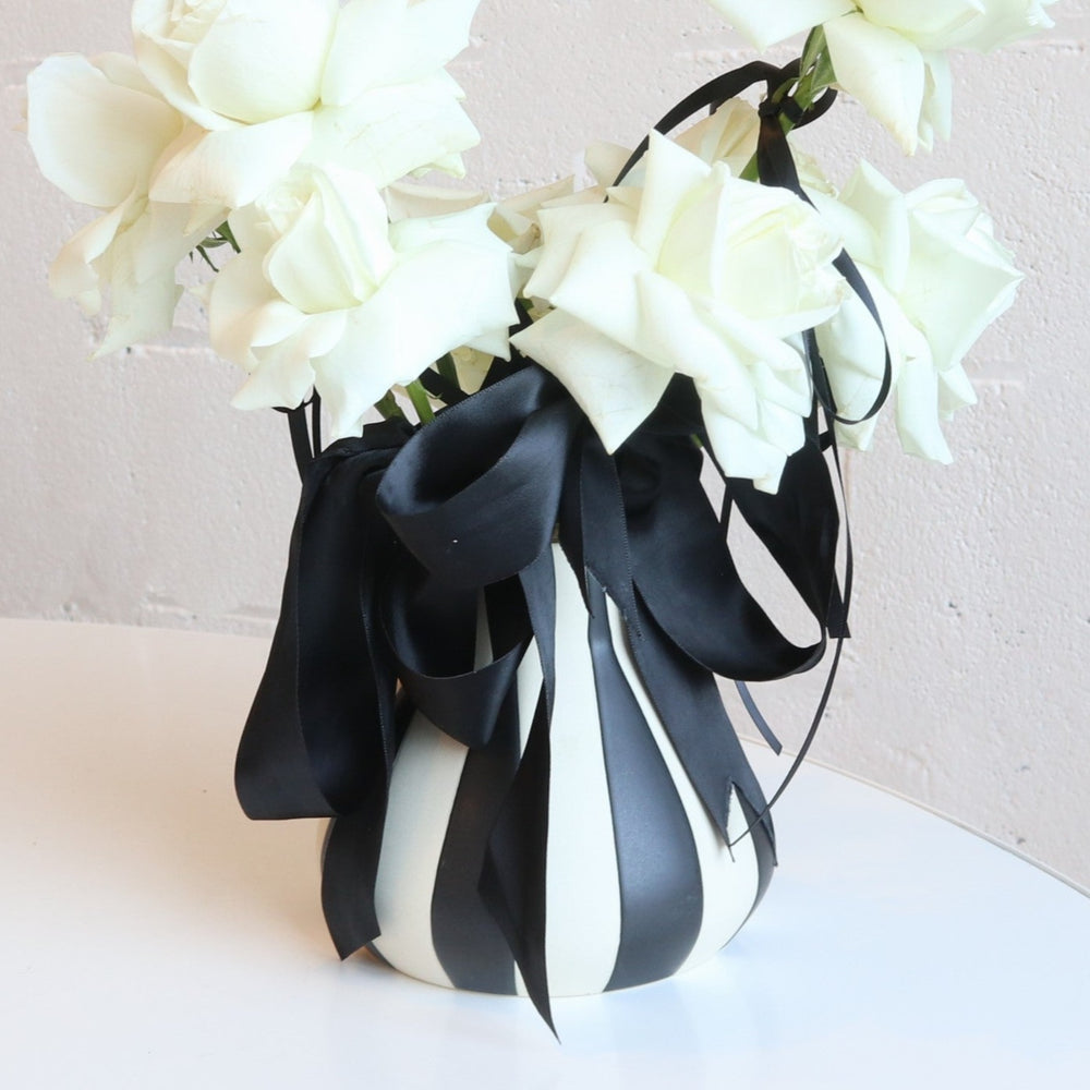 black and white striped vase with white roses accented with black ribbon.