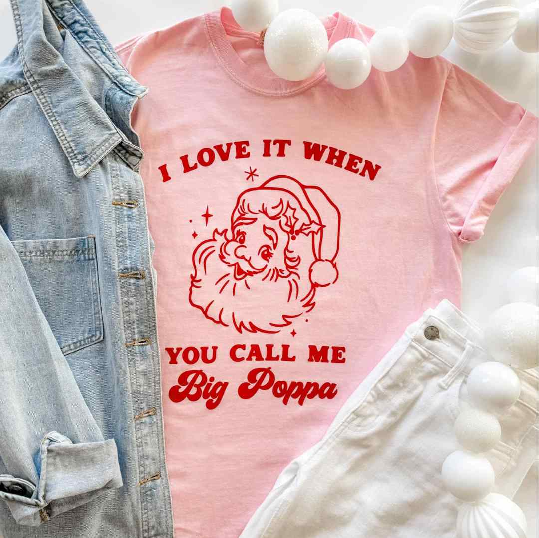Mugsby | Big Poppa Shirt | A pink shirt with red text and Santa Clause illustration. Text "I Love it when you call me Big Poppa".
