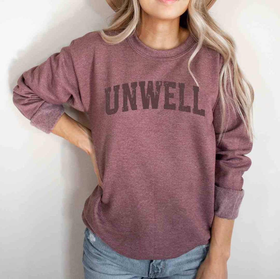Mugsby | Unwell Crewneck Sweatshirt | A maroon/pink sweatshirt with text that reads "Unwell".