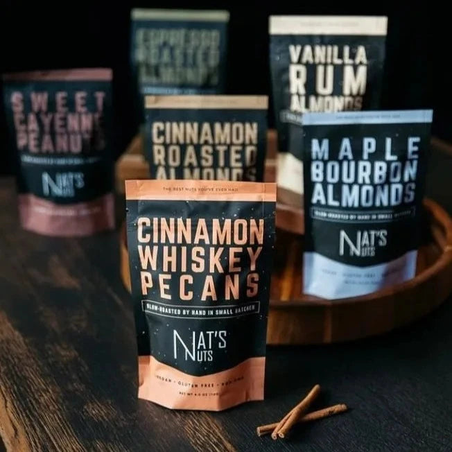 Nat's Nut's Assorted | Nat's Nuts | 6 bags of nuts against a dark background. Sweet cayenne Peanuts, espresso roasted almonds, vanilla rum almonds, cinnamon roasted almonds, maple bourbon almonds, cinnamon whiskey pecans.