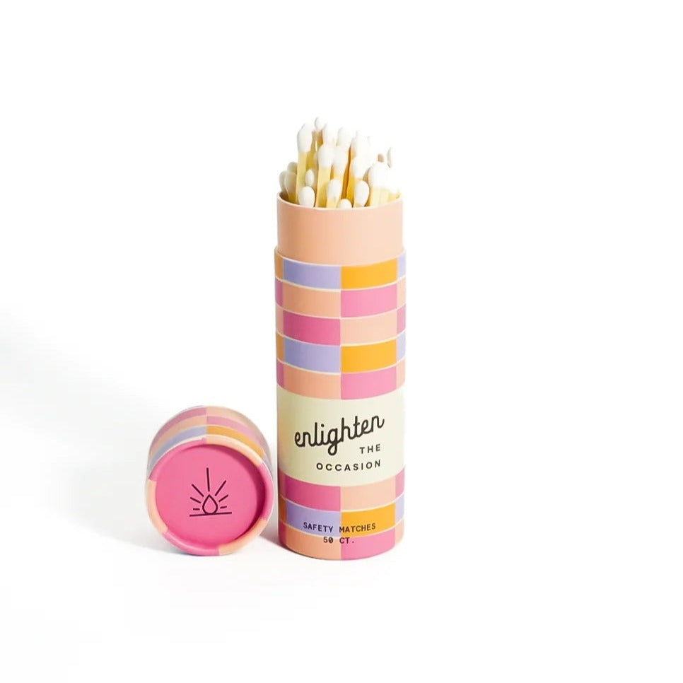 Pink Sunrise Match Tube | A pink, peach, violet, and yellow rectangle checkered pattern decorates the packaging. Text reads "Enlighten the Occasion, safety matches, 50 ct.". The matches are white.