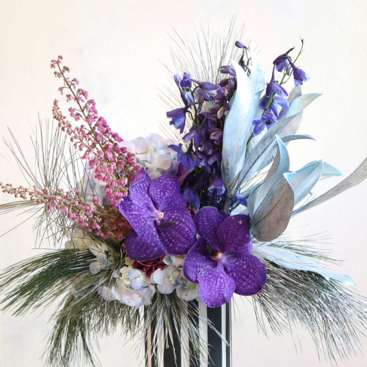 Vased flower arrangement, purple vanda orchids, painted magnolia, blue delphinium, hydrangea, silver white pine.