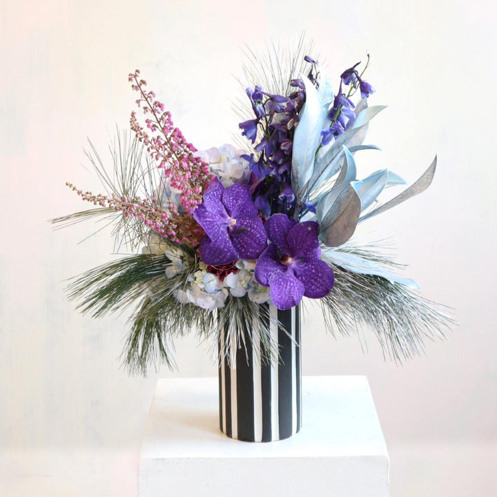 Vased flower arrangement, purple vanda orchids, painted magnolia, blue delphinium, hydrangea, silver white pine.