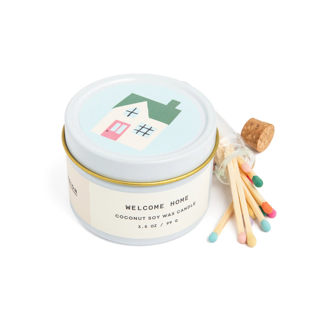 Welcome Home Tin Candle & Match Set | A scented candle with multi colored matches. Tin is decorated with a house illustration and the text reads "Welcome Home, coconut soy wax candle, 3.5 oz / 99 G.