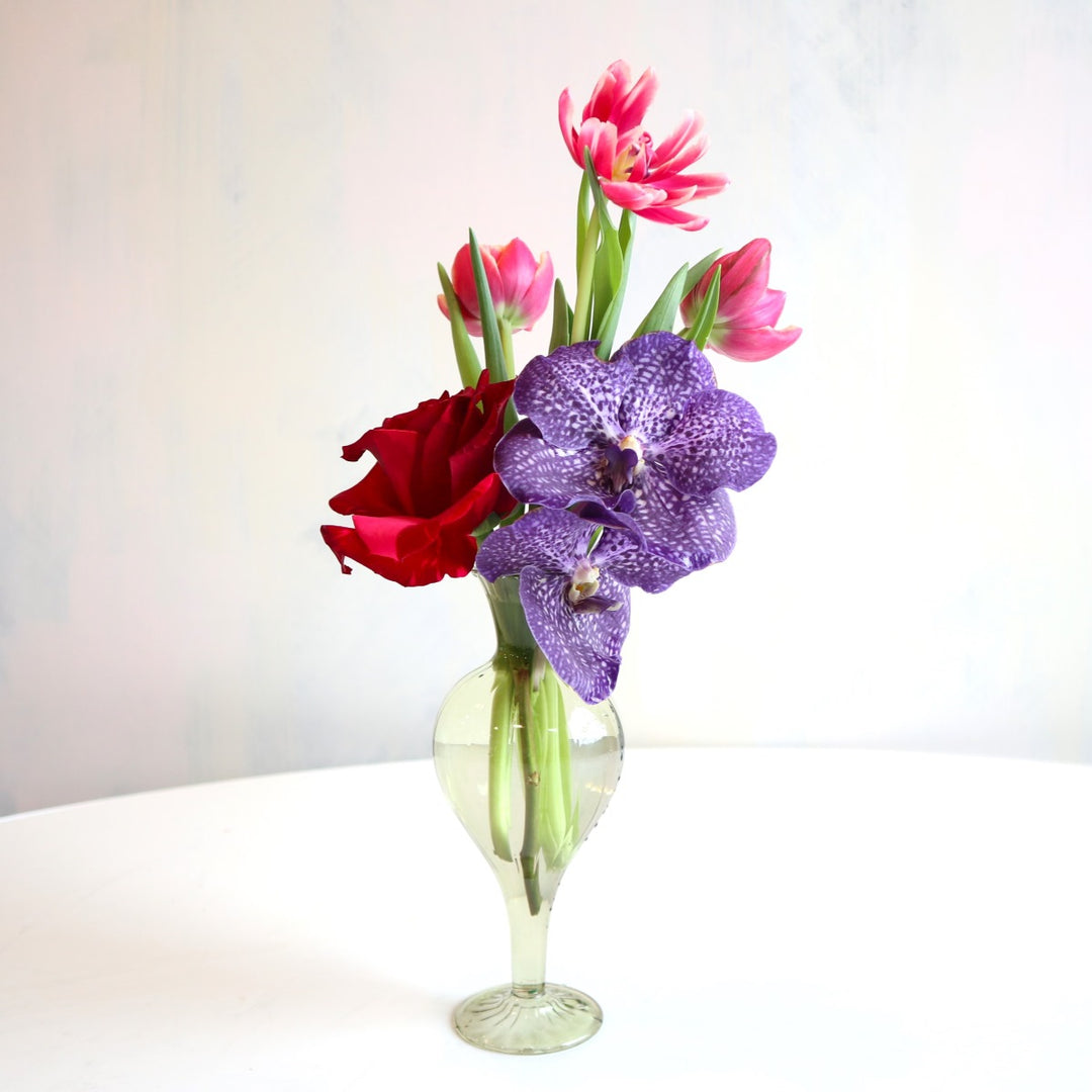 Rose, orchids, and other florals in a budvase.