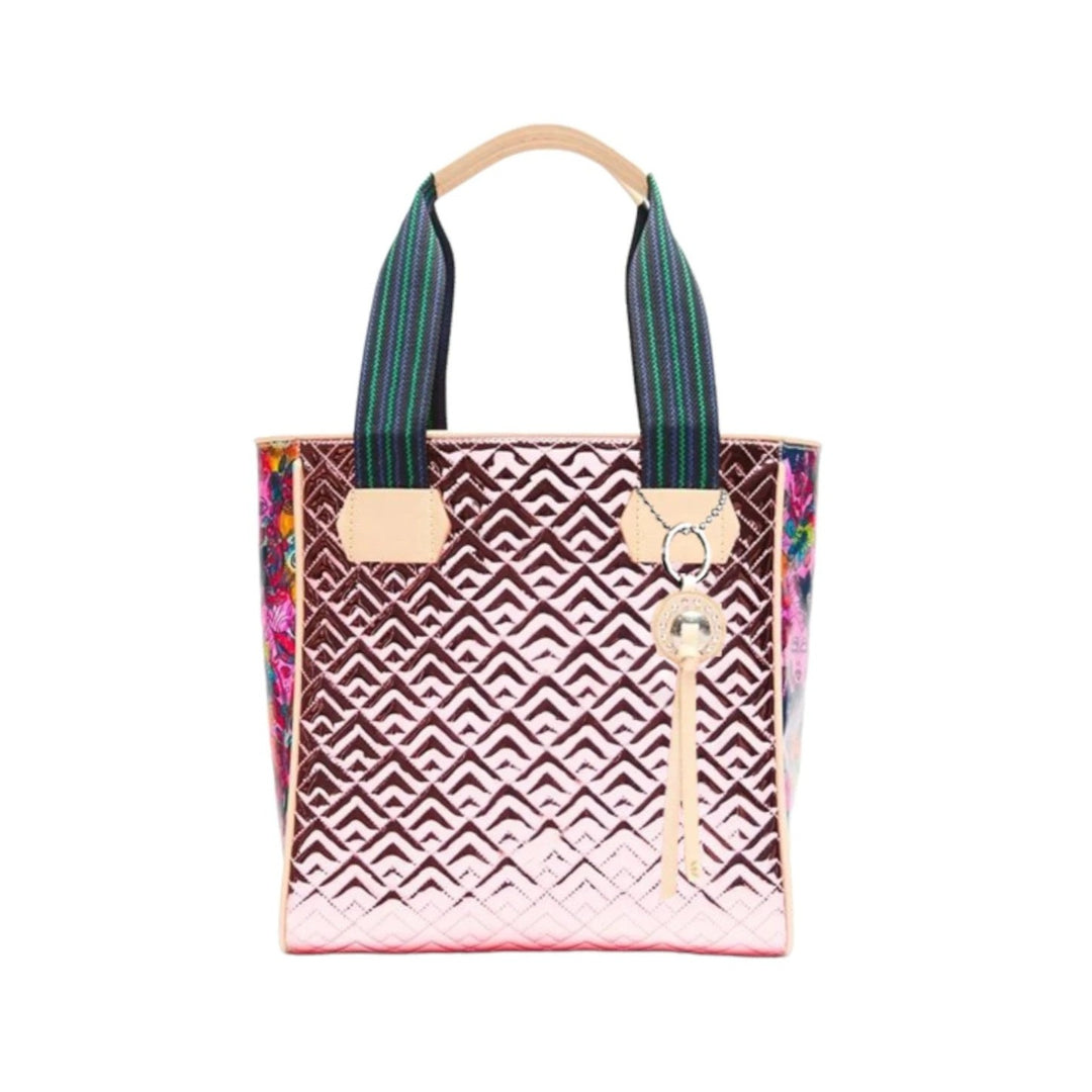 Quinn Classic Tote | Consuela | A shimmering pink bag with a geometric pattern, colorful floral sides, and a blue/green striped handle. Accented with Deigo leather.