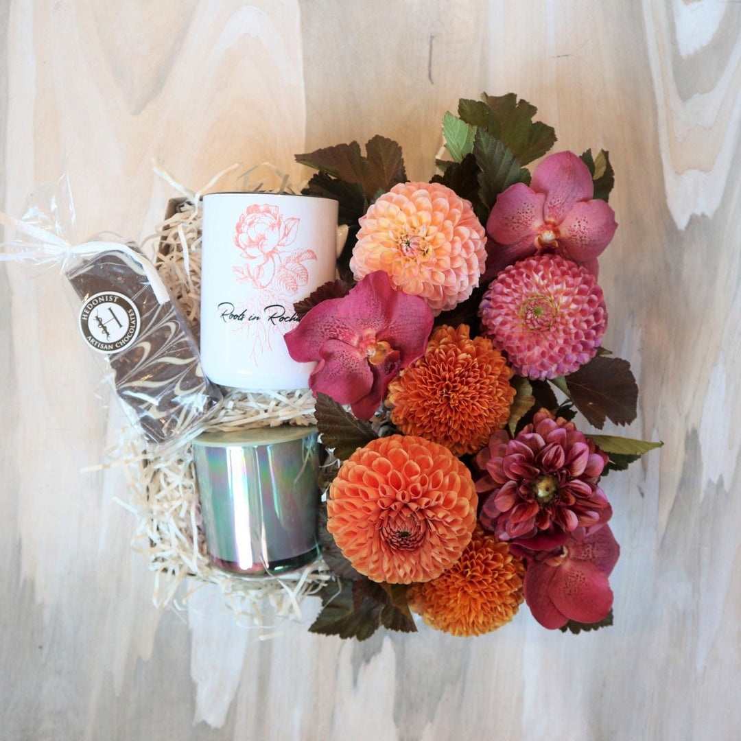 Roc Fall Gift Box | A pink and orange floral arrangement with a roots in Rochester mug, Fleurish co. candle, and Hedonist Artisan Chocolate.