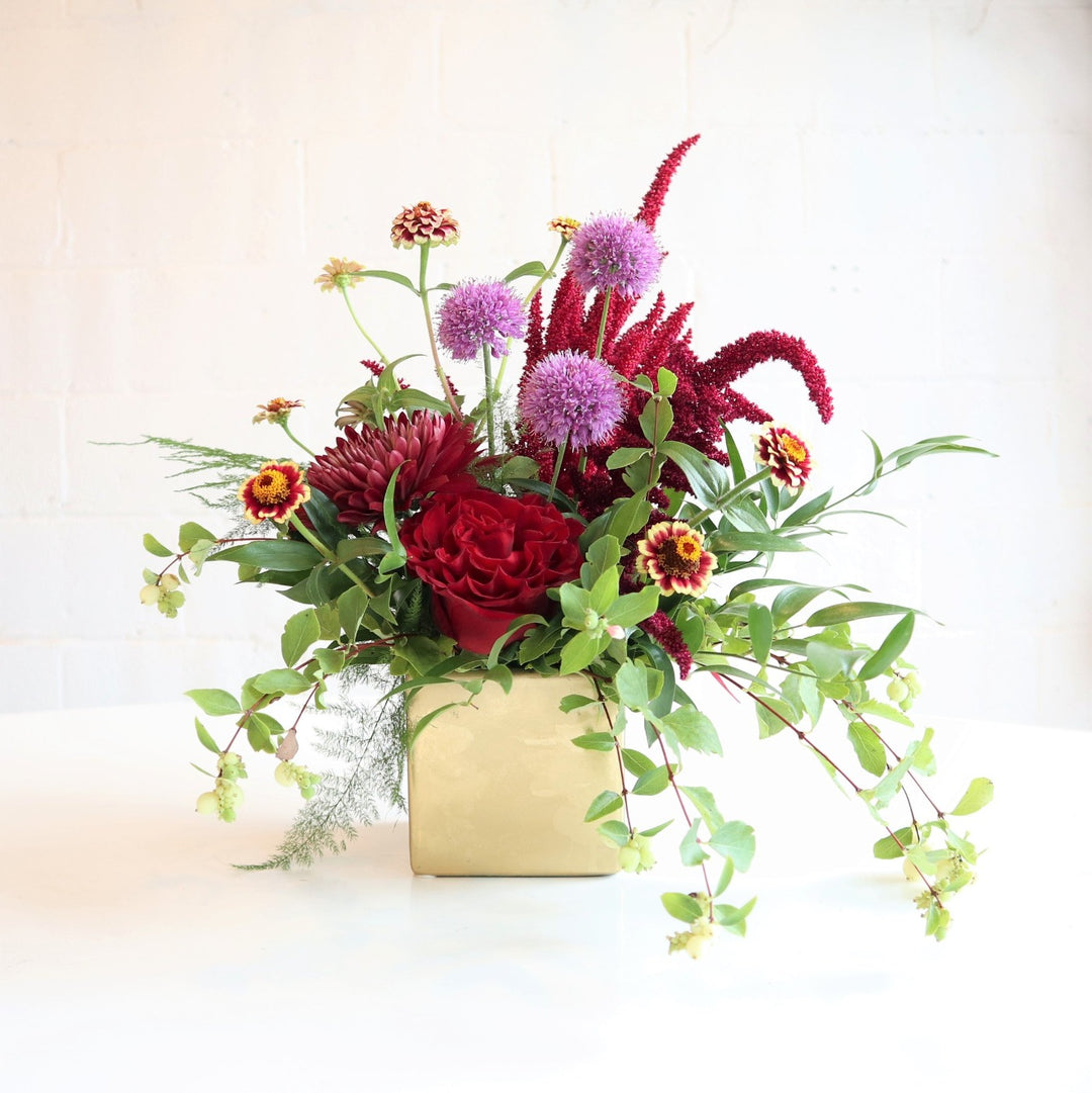 Charming | An asymmetrical arrangement with green, red, purple, and accents of yellow. In a reflective gold vase. 