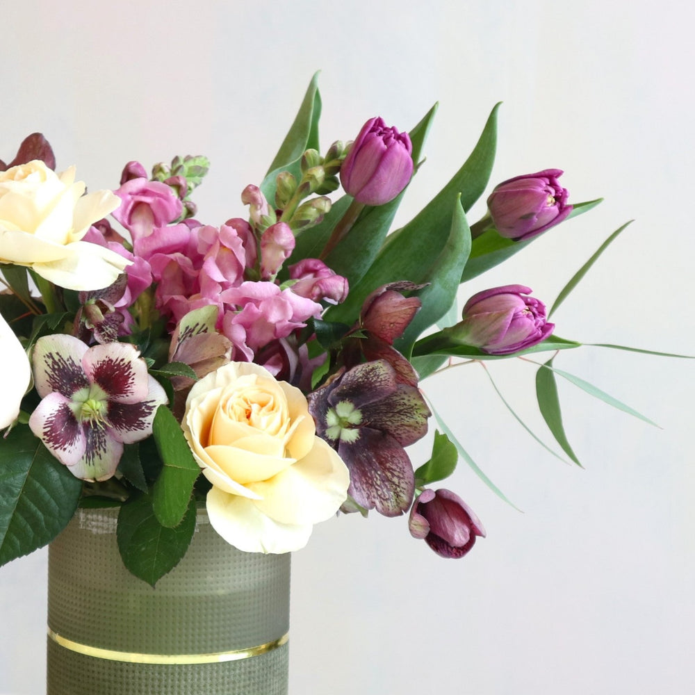 Close up of flower arrangement with purple tulips, purple snapdragons, cream roses and greenery.