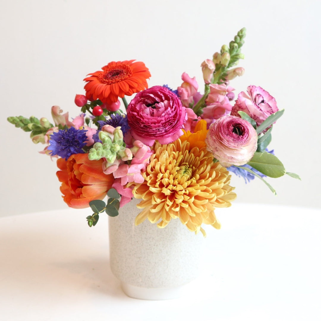 Flower arrangement with pink ranunculus, orange gerbera daisy, pink snap dragons, peach mum, orange tulips. 