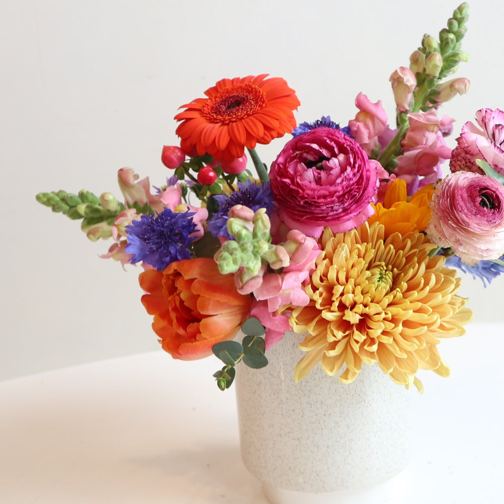 Flower arrangement with pink ranunculus, orange gerbera daisy, pink snap dragons, peach mum, orange tulips.