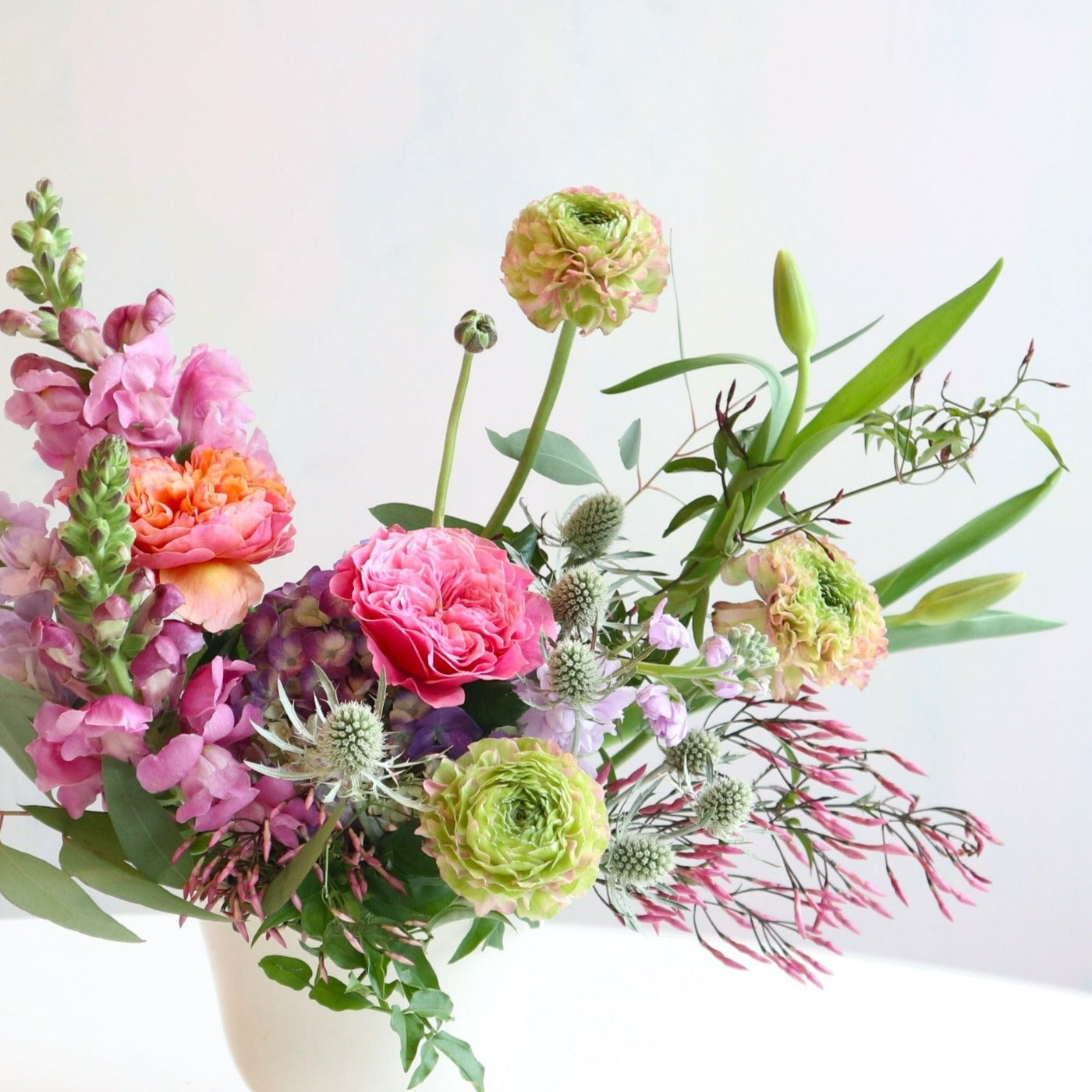 Enchanted | Close up on the arrangement of pinks, purples, and greens in a white vase.