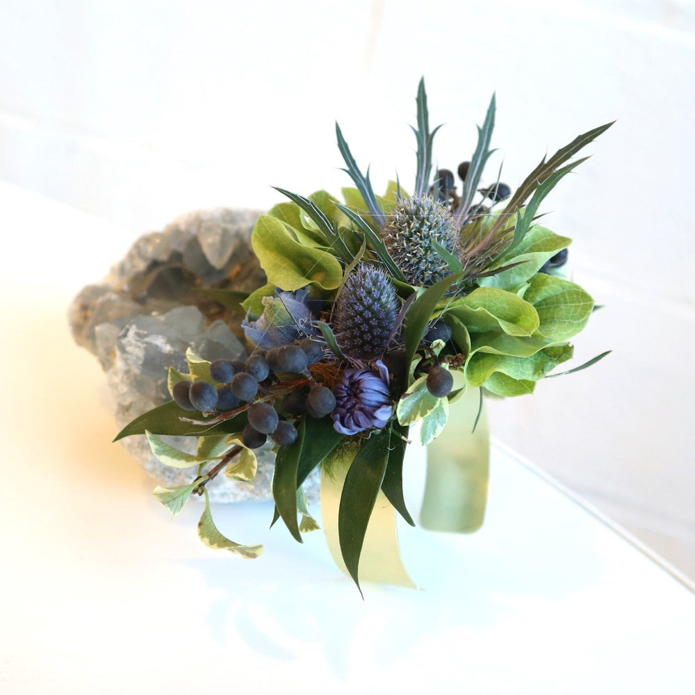 A corsage with bits of bells of ireland, blue thistle, blue berries and hints of blue mums.