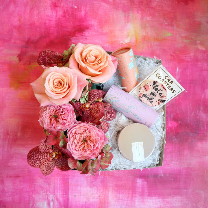 Galentine's Day Box. Included in the box is a set of car coasters for your cup holders, a studio exclusive candle from Fleurish,  cocktail cubes for drinks and a beautiful custom designed floral arrangement. The floral arrangement has dark pink orchids, coral roses and antique hydrangea.