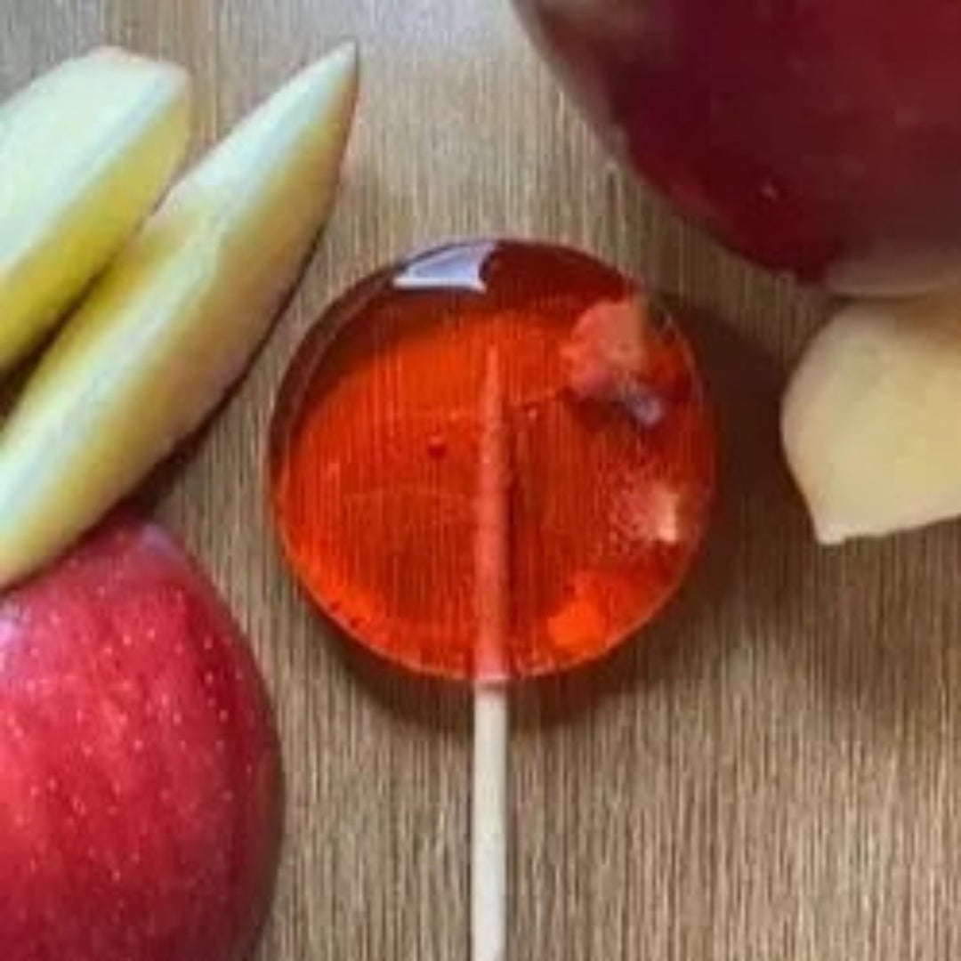 Good Lolli Candy Apple Lollipop. Red lollipop with apple chunks inside. Photo taken on wood background with apple slices placed decoratively around.