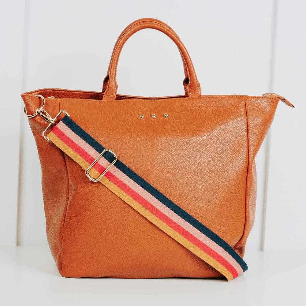Kaia Vegan Leather Travel Bag | A brown travel bag with a simple brown handle and a multi color (Yellow, dark pink, light pink, and navy blue) striped strap that can be over the shoulder or crossbody.