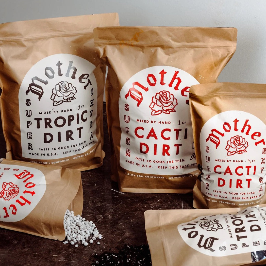 Plant Dirt | Mother Co. | Photo by Planty Queens | Photo shows 4 bags of dirt, each labeled either Mother Tropic Dirt, or Mother Cacti Dirt. The bags are brown with a white label and either red or brown text with an illustrated rose in the front.