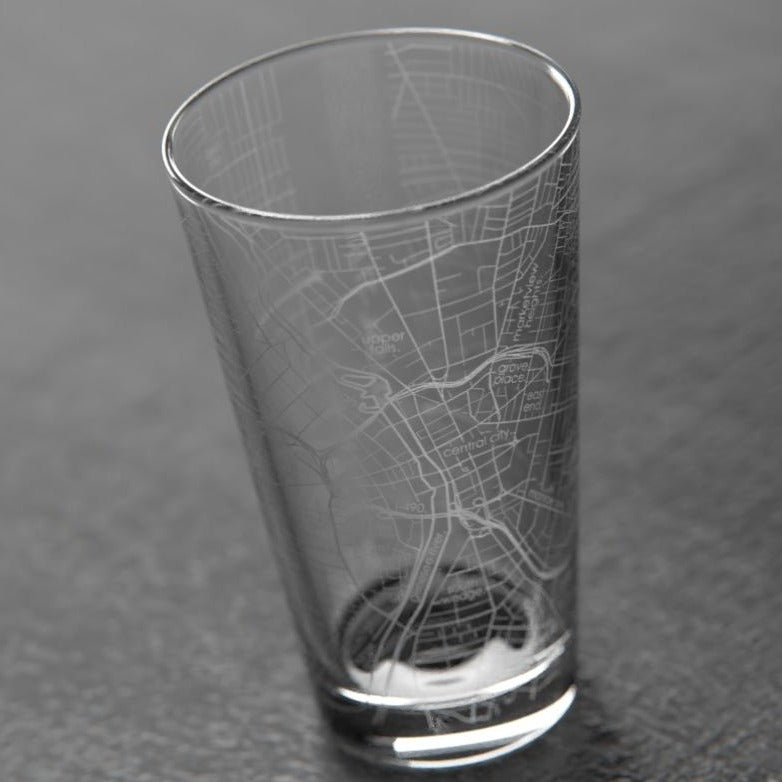 Rochester NY Pint Glass | A transparent pint glass with the map of Rochester NY printed on. Photo taken against a dark slate background.