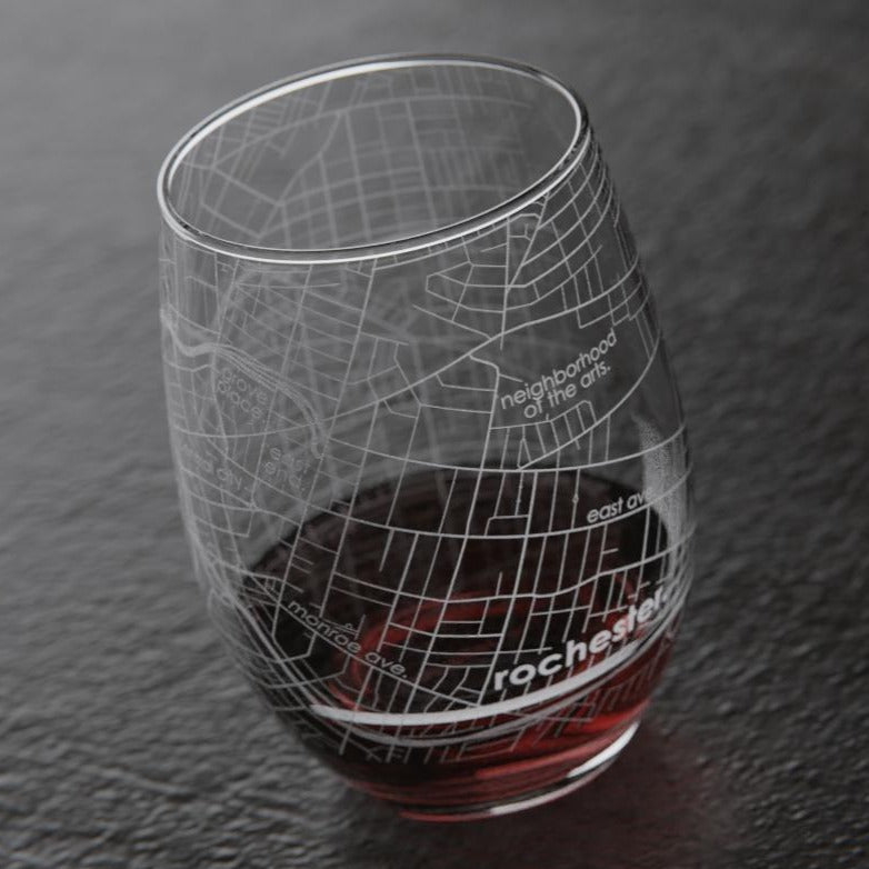 Rochester Stemless Wine Glass | A transparent wine glass with the streets of Rochester NY printed on. This side of the glass show the neighborhood of the arts, east ave, monroe ave, and all the roads in between. Photo is taken of the wine glass with a little wine in the bottom, against a dark surface.