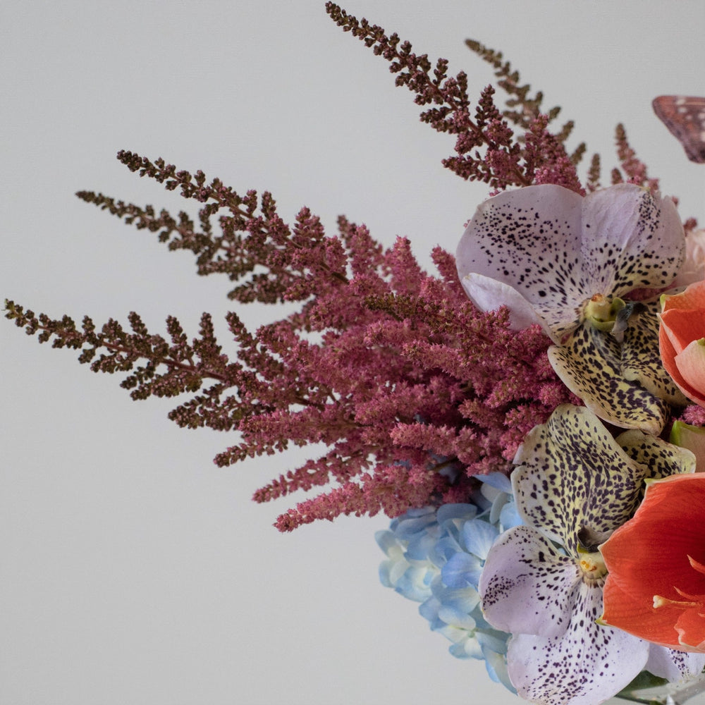 Whymsical floral arrangment with butterflies. Transparent bowl vase with Orchids, blue hydrangea, and decorative butterflies. Close up on pink astilbe.
