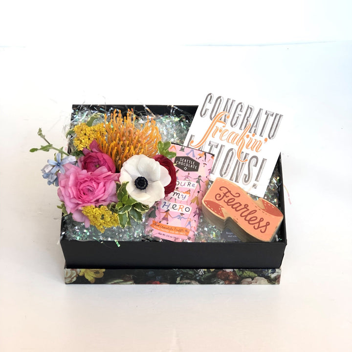 Gift Box featuring a small floral arrangement, Seattle Chocolate "You're My Hero" bar, "Congratu-freakin'-lations!" Card, and small wood block "Fearless" sign.