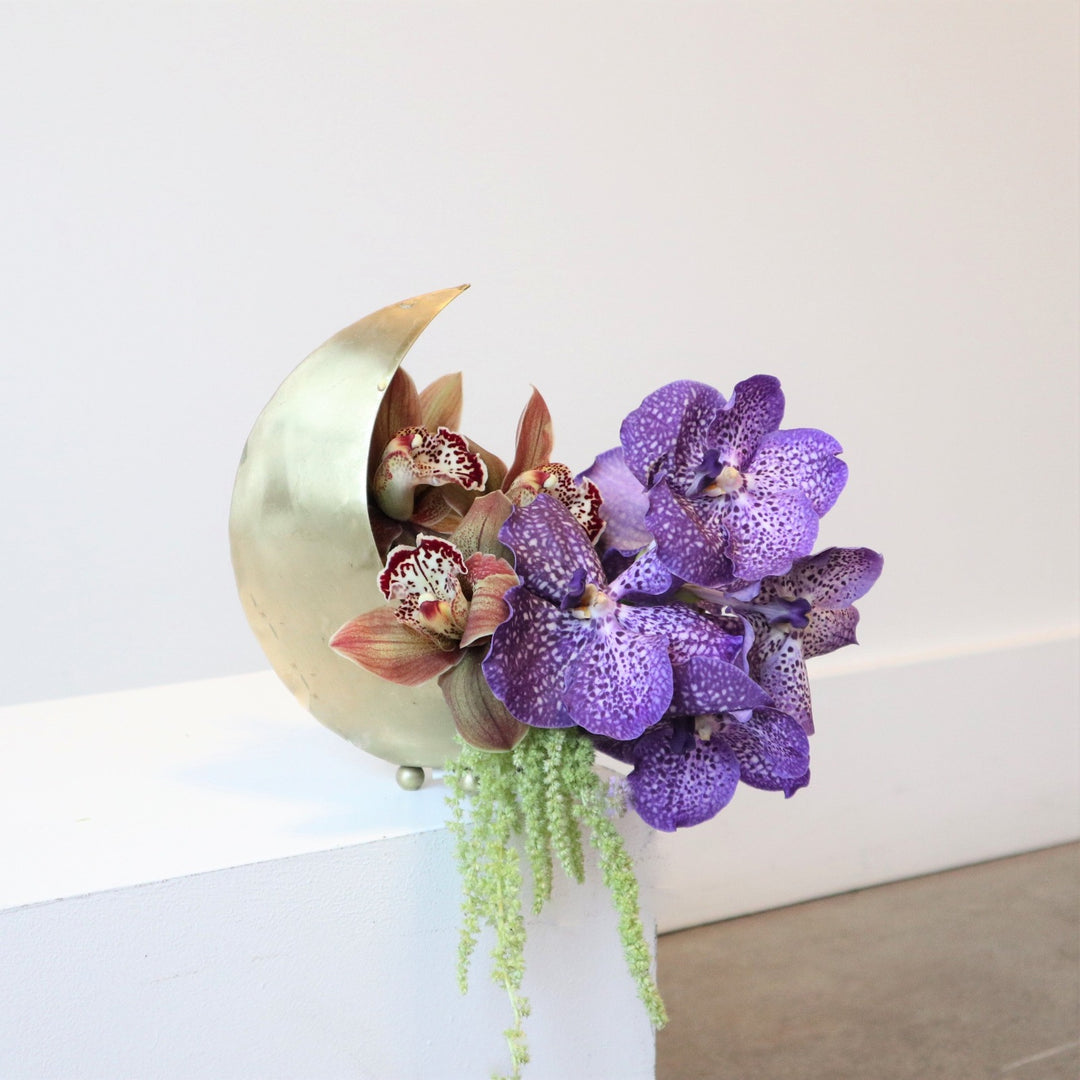 Arrangement with purple and red orchids with green ameranthus in a gold cresent shaped moon planter.