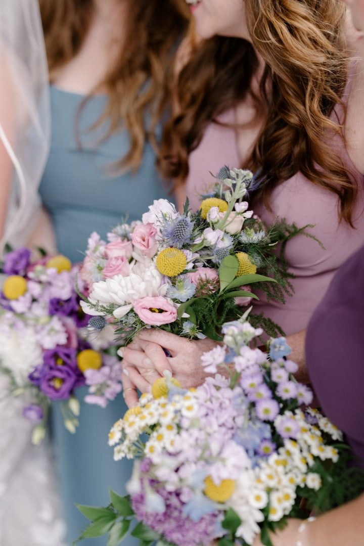 Bridal party holding whimsical purple bouquets with spray roses, gerber daisies, billy balls, mums, and more.