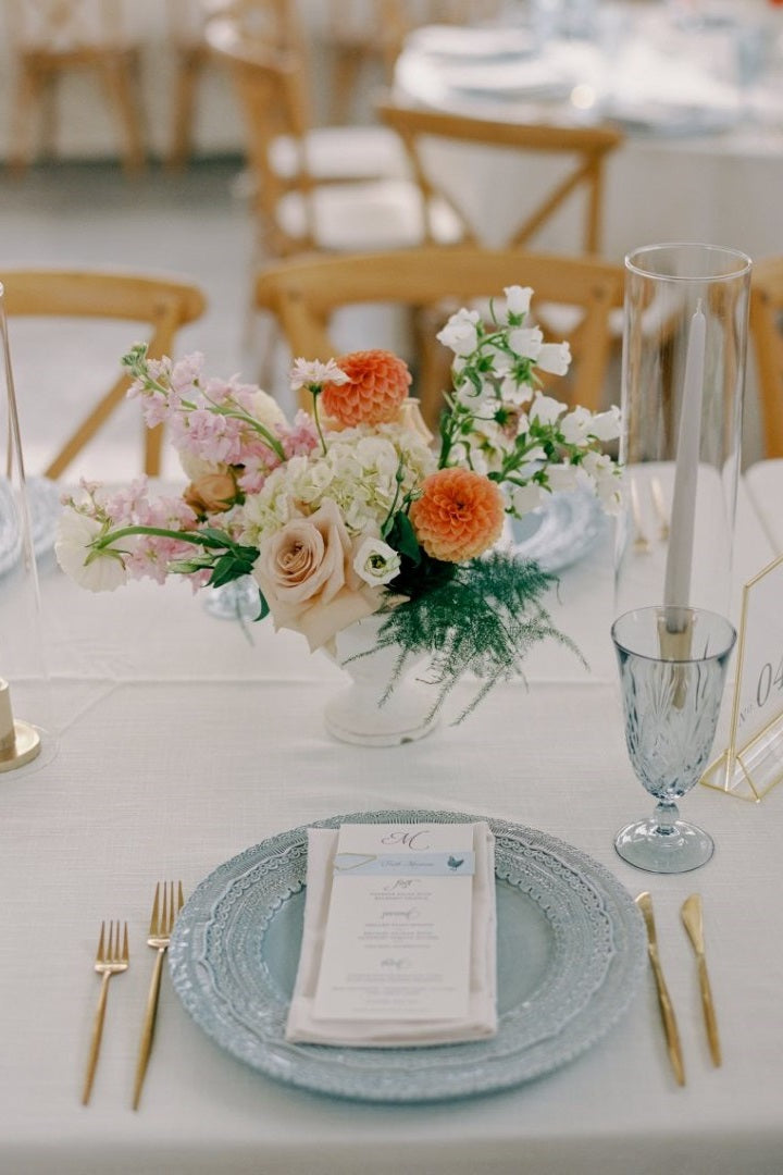 A orange, pink, and cream, floral arrangement with fern greenery.