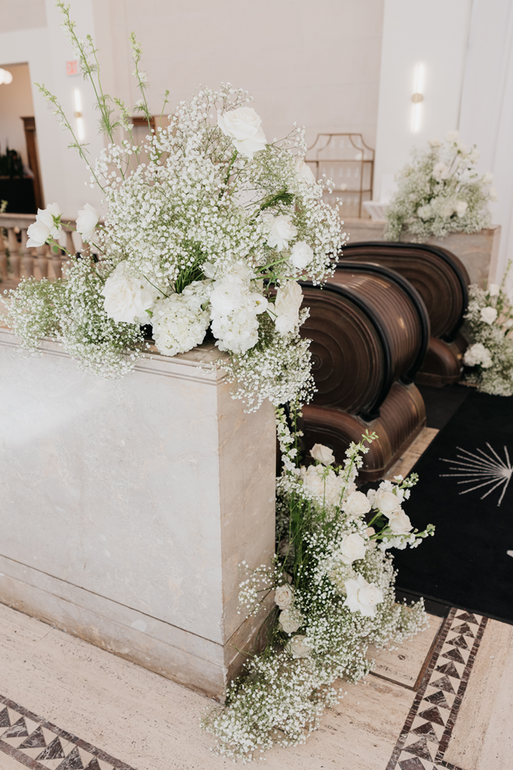 Soft green and white floral arrangements with babies breath and roses. Placed next to escalator stairs.