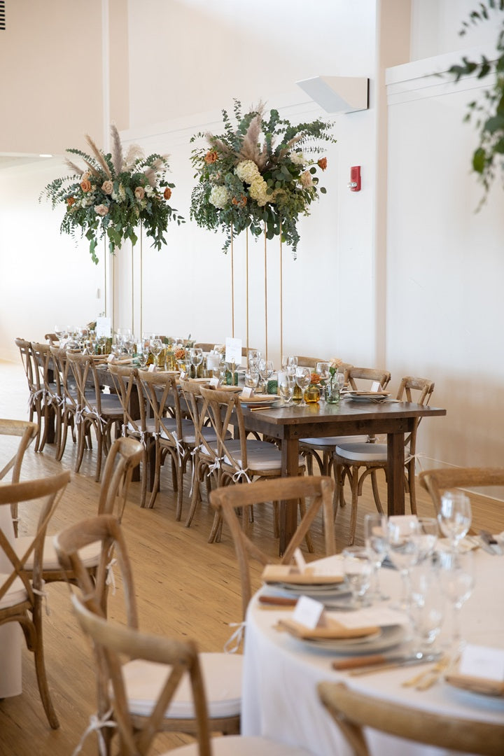 Reception tables with loose greenery, bud vases, and elevated floral/greenery centerpieces.