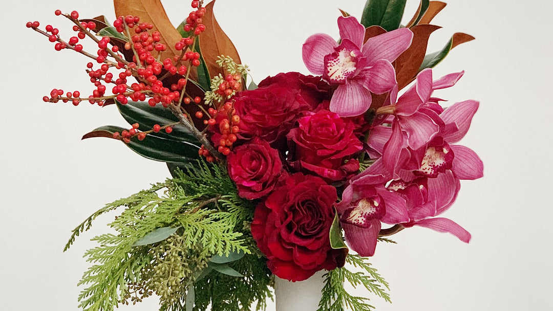 Roses orchids berries and winter greens in a white vase 