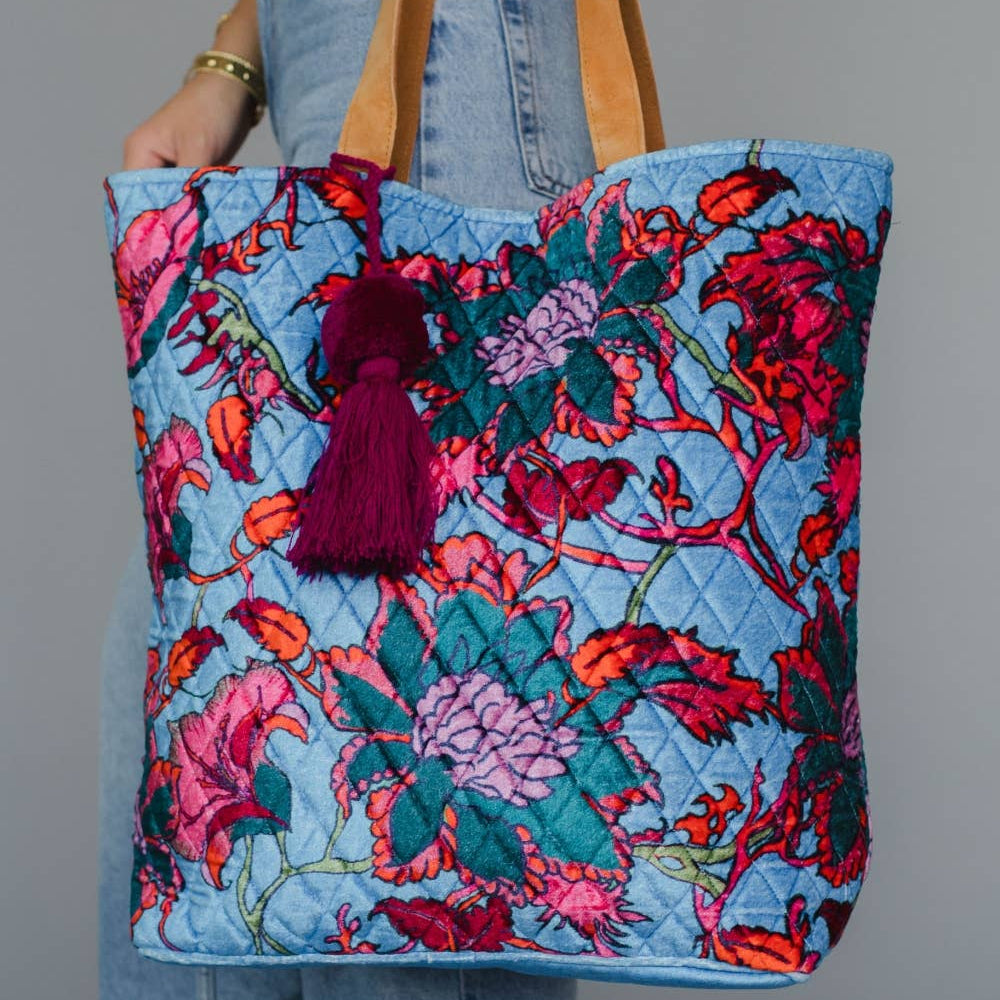 Floral tote bag with tassel held by a person wearing jeans against a gray background