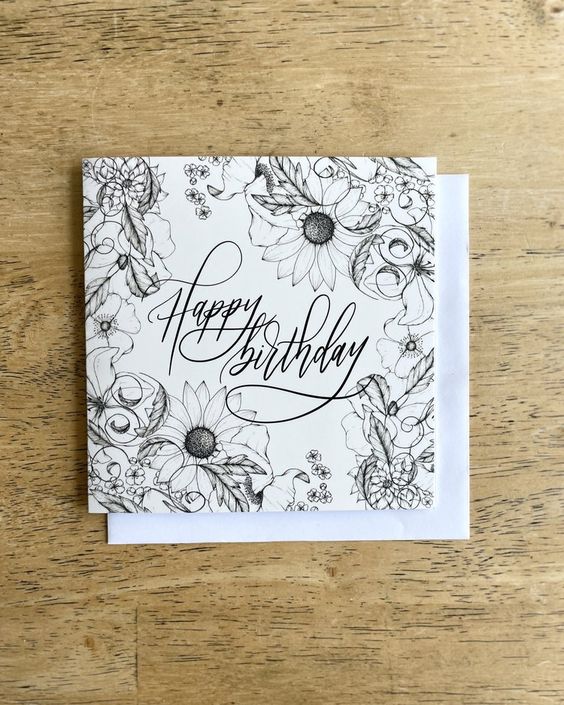 A charming white square greeting card with illustrations of wildflowers and a lettered message "Happy Birthday".