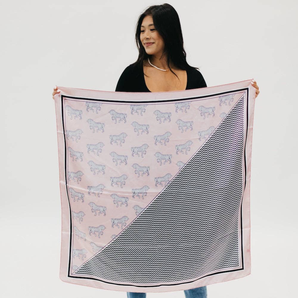 Model holding up a light pink hair scarf that is half horse themed and half striped pattern.