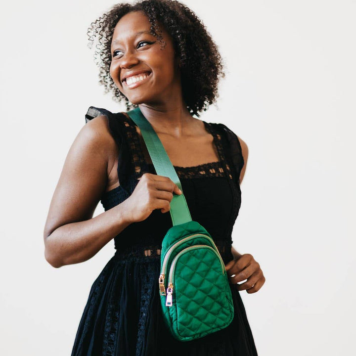 An emerald crossbody bag with a quilted texture held by a model in a black dress.