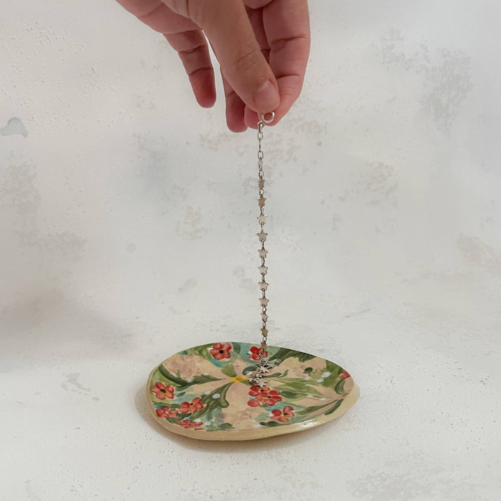 Andrea Durfee | Petite Floral Dishes | A green, pink, and red, floral dish with a model placing a necklace on it.