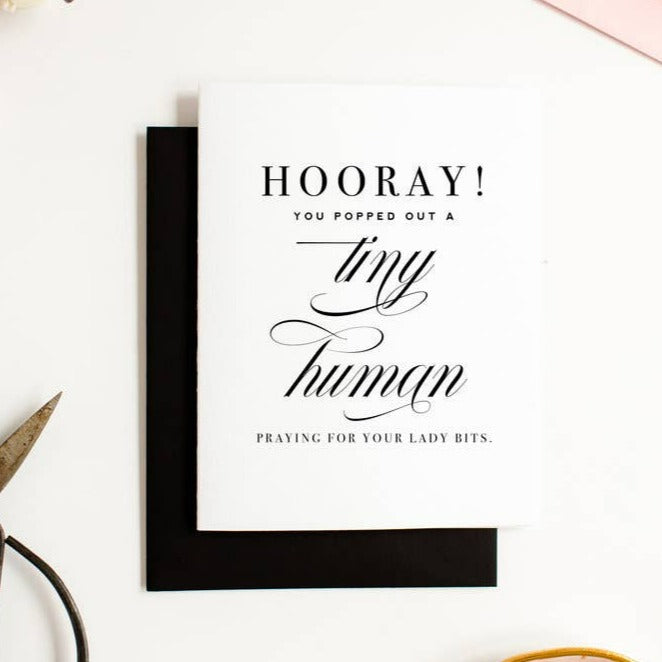 A simple white card with black text that reads "Hooray! You popped out a tiny human. Praying for your lady bits." Comes with a simple black envelope.