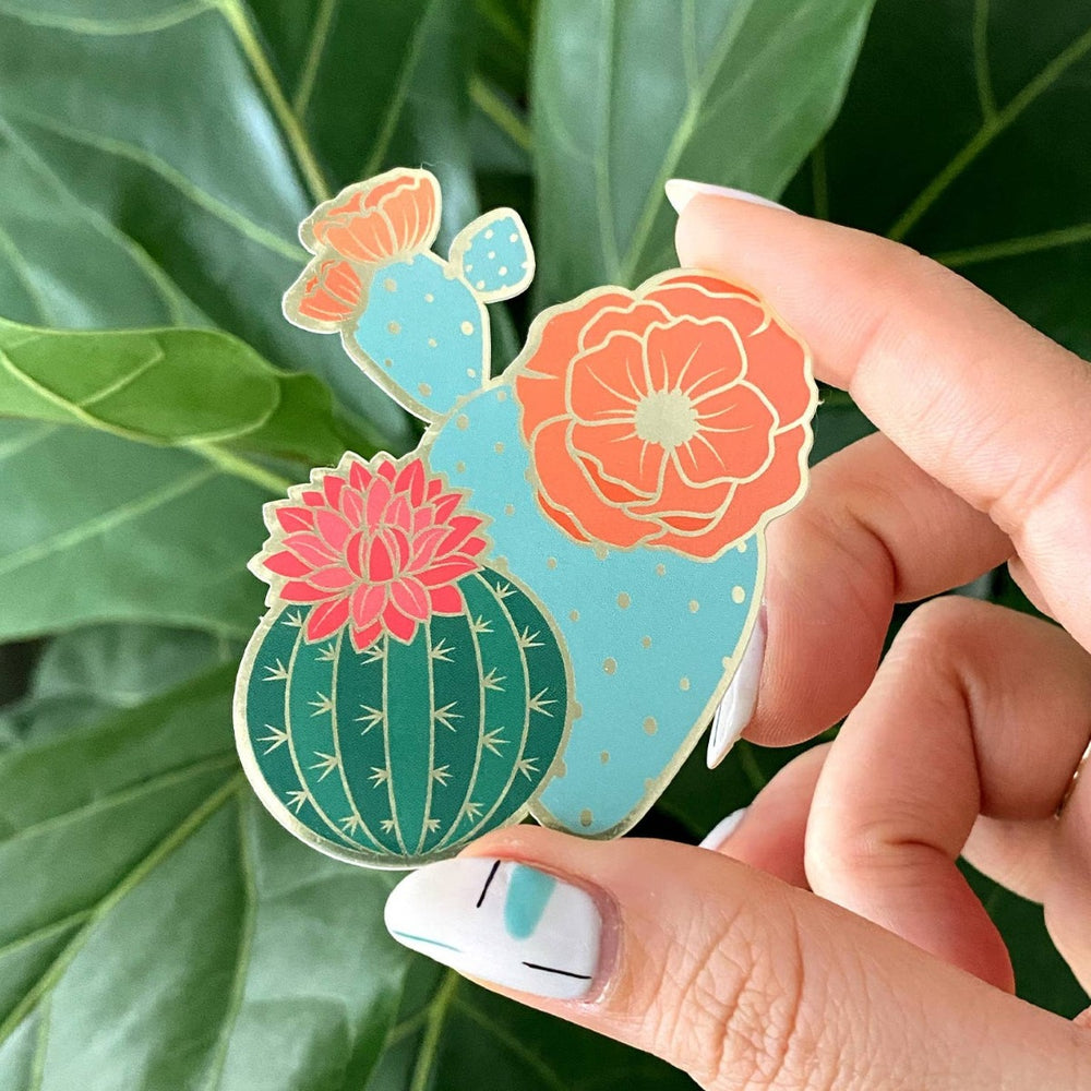Blooming Cacti Sticker | Close up on the gold accented colorful cacti sticker. It is being held in front of a live plant.