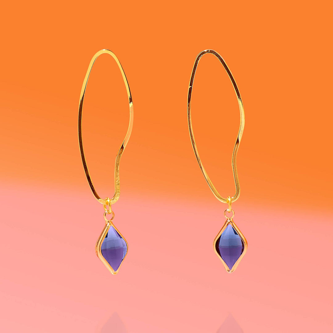 Gold earrings with purple gemstones on a gradient orange to pink background