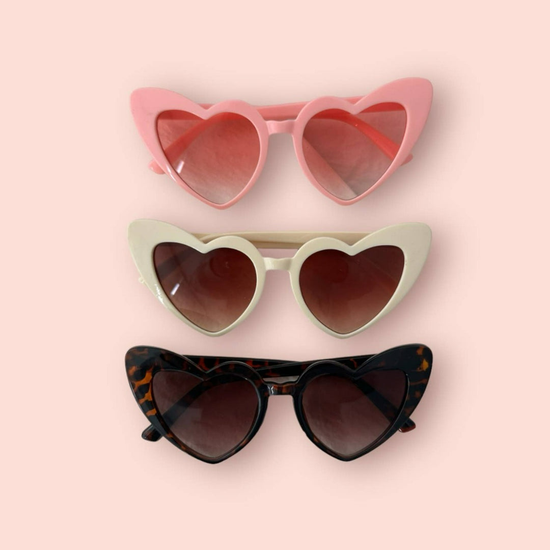 Three pairs of heart shaped glasses in the colors pink, white, and black/brown.